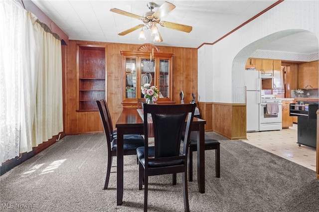 917 Park Ave SW, Canton, OH 44706 - dining room featuring wooden walls, arched walkways, light colored carpet, ceiling fan, and ornamental molding
