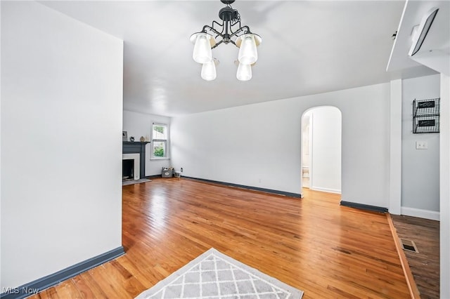 2506 Bears Den Rd, Youngstown, OH 44511 - unfurnished living room with arched walkways, a chandelier, light wood-type flooring, baseboards, and a fireplace with flush hearth