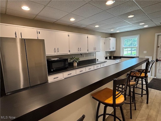1931 King James Unit 131, Westlake, OH 44145 - kitchen with black microwave, freestanding refrigerator, white cabinetry, dark countertops, and a breakfast bar area