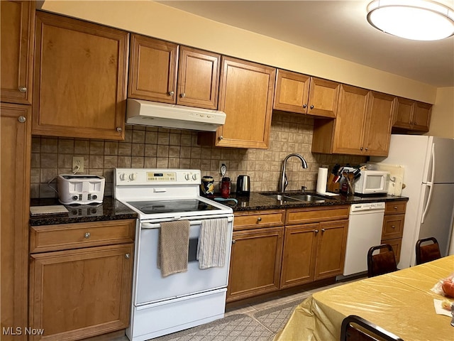 12701 Gordon St, North Royalton, OH 44133 - kitchen featuring white appliances, under cabinet range hood, brown cabinetry, tasteful backsplash, and dark stone counters