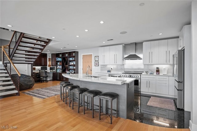 701 W Lakeside Ave Unit Ph-2A/1302, Cleveland, OH 44113 - kitchen with wall chimney range hood, appliances with stainless steel finishes, a sink, light wood-style flooring, and a kitchen bar