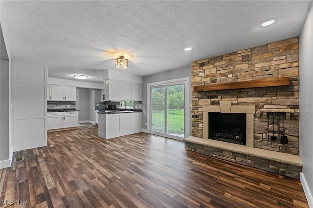 3371 Padanarum Rd, Geneva, OH 44041 - unfurnished living room featuring a textured ceiling, dark wood-type flooring, a stone fireplace, baseboards, and a sink