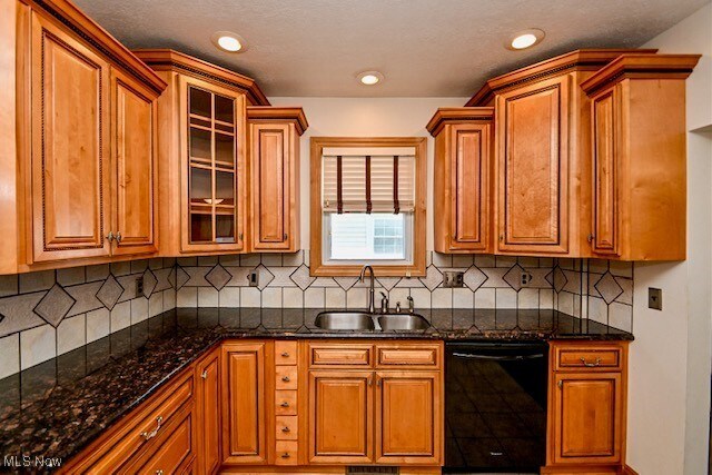 837 Lake Ave NE, Massillon, OH 44646 - kitchen featuring dishwasher, a sink, brown cabinetry, glass insert cabinets, and dark stone countertops