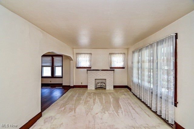 837 Lake Ave NE, Massillon, OH 44646 - unfurnished living room with arched walkways, a brick fireplace, and baseboards