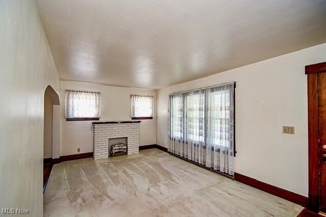 837 Lake Ave NE, Massillon, OH 44646 - unfurnished living room featuring arched walkways, carpet floors, baseboards, and a fireplace