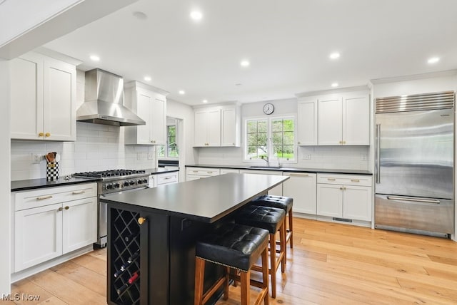 19 Brandywood Dr, Pepper Pike, OH 44124 - kitchen with high quality appliances, wall chimney exhaust hood, dark countertops, light wood-style flooring, and white cabinets