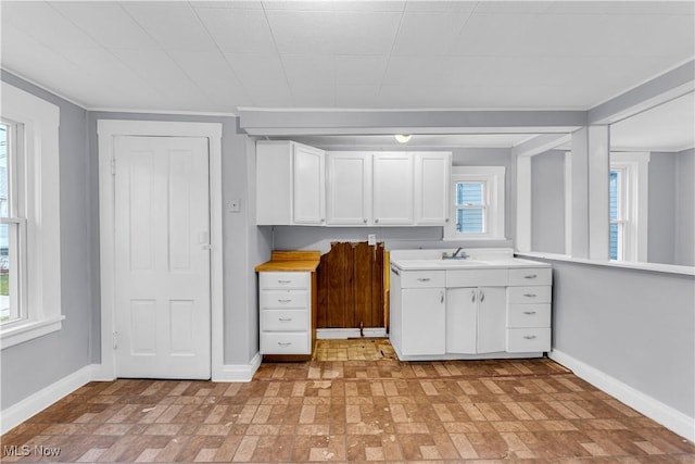 4611 W 41st St, Cleveland, OH 44109 - kitchen featuring baseboards, brick patterned flooring, white cabinets, light countertops, and healthy amount of natural light