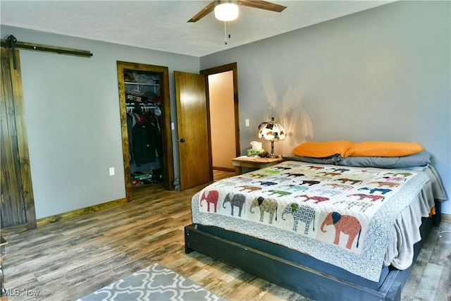 6416 Wilson Sharpsville Rd, Fowler, OH 44418 - bedroom featuring a barn door, wood finished floors, baseboards, a spacious closet, and a ceiling fan
