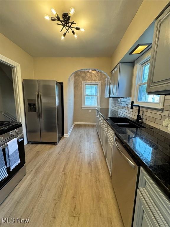 351 E 197th St, Euclid, OH 44119 - kitchen with appliances with stainless steel finishes, a sink, arched walkways, light wood-style floors, and decorative backsplash