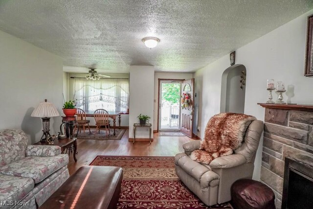 5920 Renninger Rd, New Franklin, OH 44319 - living room with a ceiling fan, wood finished floors, a textured ceiling, a stone fireplace, and arched walkways