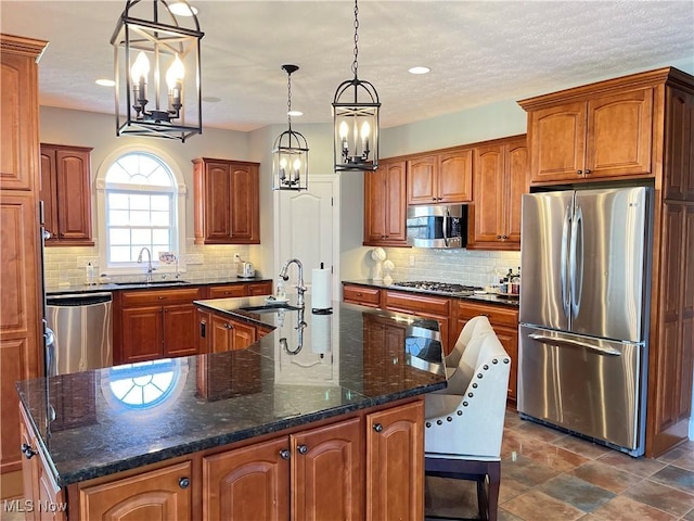 4679 Paxton Rd, Copley, OH 44321 - kitchen featuring stainless steel appliances, a chandelier, a large island with sink, backsplash, and brown cabinets