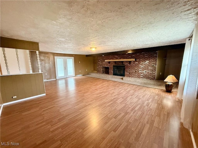 47 Walker Manor Cir, Colliers, WV 26035 - unfurnished living room with wood finished floors, a textured ceiling, a brick fireplace, and wooden walls