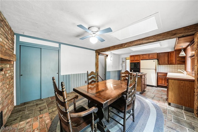 11828 Sheldon Rd, Mantua, OH 44255 - dining space featuring stone tile flooring, ceiling fan, brick wall, and a skylight