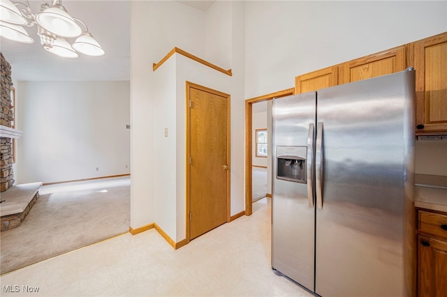 7410 Fieldstone Ave, Conneaut, OH 44030 - kitchen featuring stainless steel fridge, a stone fireplace, baseboards, brown cabinets, and light carpet
