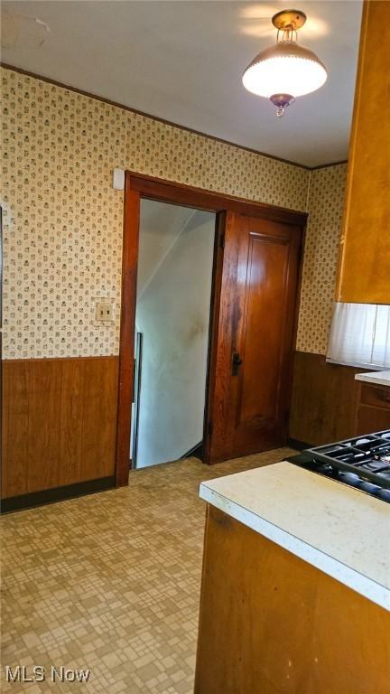 10612 Linnet Ave, Cleveland, OH 44111 - kitchen with light countertops, brown cabinetry, a wainscoted wall, wallpapered walls, and light flooring
