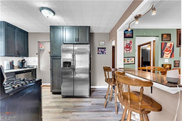 459 Lloyd Rd, Euclid, OH 44132 - kitchen with stainless steel appliances, a kitchen breakfast bar, light wood-style flooring, a textured ceiling, and tasteful backsplash