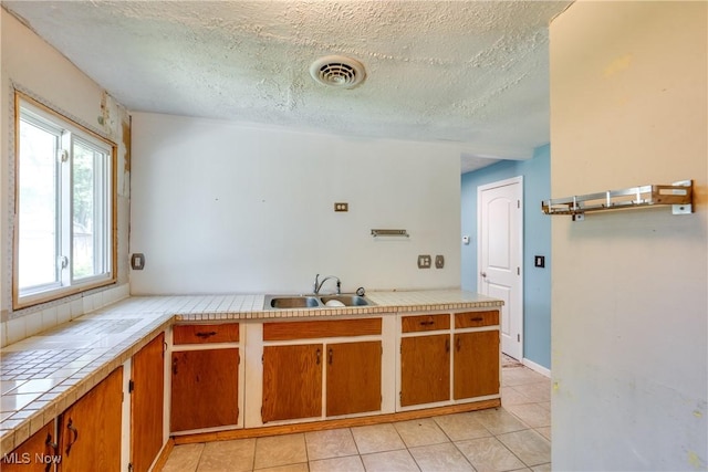 4944 Coleman Dr, Akron, OH 44319 - kitchen featuring a sink, tile counters, a textured ceiling, light tile patterned floors, and brown cabinets