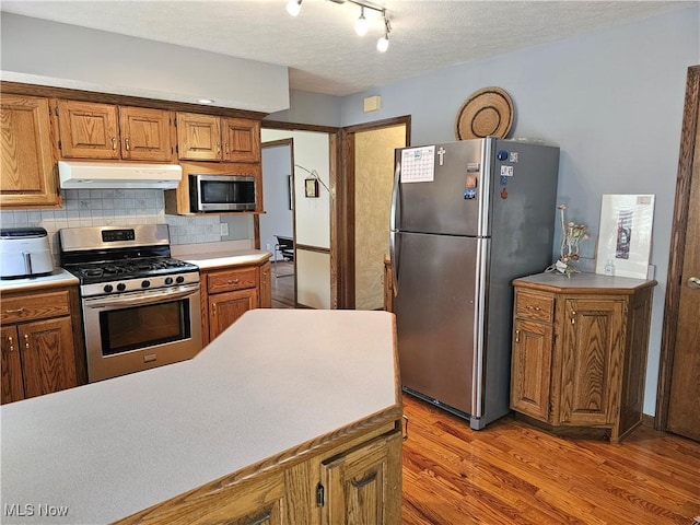 6671 Queens Way N, Royalton, OH 44133 - kitchen with stainless steel appliances, under cabinet range hood, light wood-style flooring, decorative backsplash, and brown cabinetry