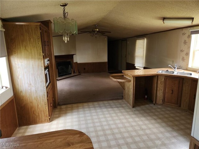 723 Mulvane, Newcomerstown, OH 43832 - kitchen featuring a sink, a textured ceiling, a fireplace with raised hearth, light flooring, and brown cabinets