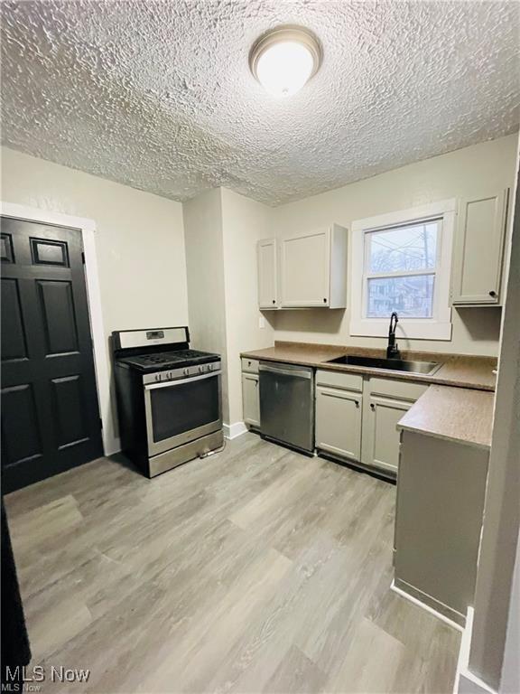 2511 4th St NW, Canton, OH 44708 - kitchen featuring appliances with stainless steel finishes, a textured ceiling, a sink, light wood finished floors, and white cabinetry