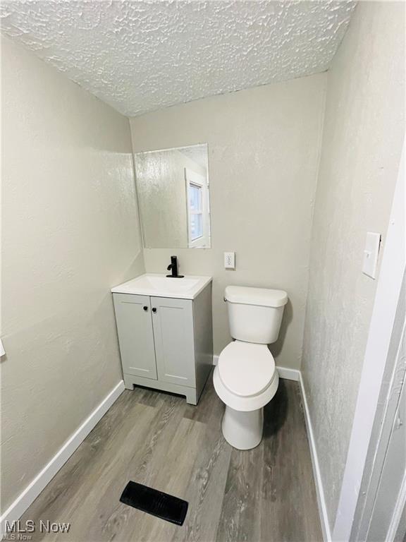 2511 4th St NW, Canton, OH 44708 - bathroom with vanity, wood finished floors, toilet, a textured ceiling, and baseboards
