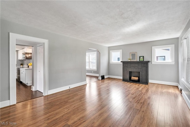 990 Franklin Ave, Salem, OH 44460 - unfurnished living room with arched walkways, wood finished floors, a fireplace, a textured ceiling, and baseboards