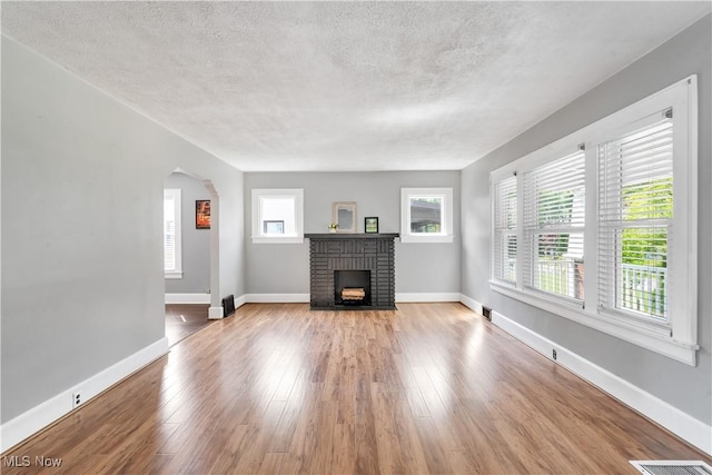 990 Franklin Ave, Salem, OH 44460 - unfurnished living room featuring a brick fireplace, arched walkways, a textured ceiling, plenty of natural light, and wood finished floors