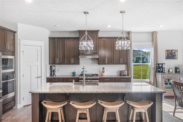 34655 N Legends Way, Grafton, OH 44044 - kitchen featuring under cabinet range hood, stainless steel appliances, a breakfast bar, dark brown cabinets, and light wood-style floors