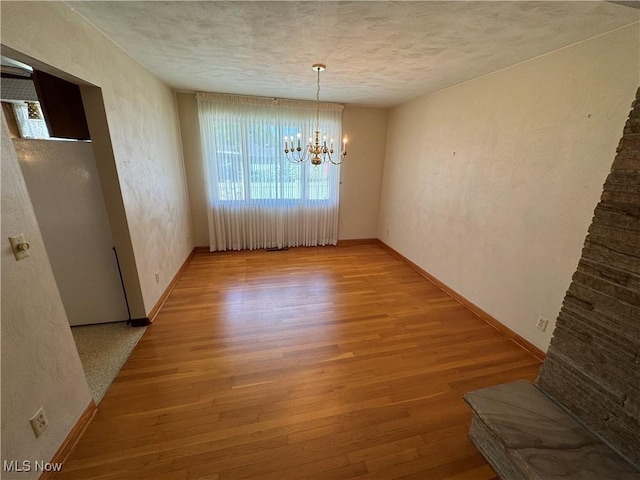 158 Main St, Rayland, OH 43943 - unfurnished dining area with a chandelier, light wood-style floors, baseboards, a textured ceiling, and a textured wall