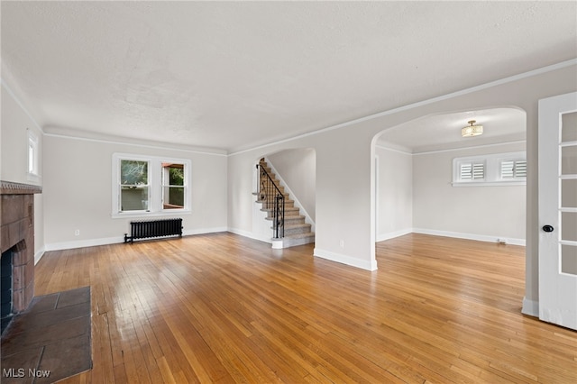 3497 Raymont Blvd, University Heights, OH 44118 - unfurnished living room with radiator, arched walkways, stairs, a tiled fireplace, and light wood-style floors