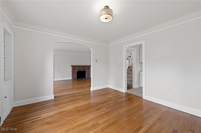 3497 Raymont Blvd, University Heights, OH 44118 - unfurnished living room featuring arched walkways, a brick fireplace, light wood-style flooring, baseboards, and stairs