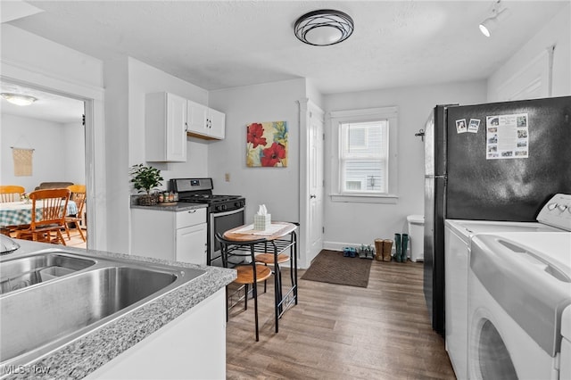 14520 Bayes Ave, Lakewood, OH 44107 - kitchen featuring stainless steel gas range oven, washing machine and clothes dryer, wood finished floors, a sink, and white cabinetry
