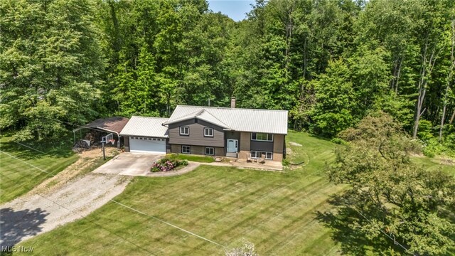 11996 Bower Rd, Minerva, OH 44657 - bi-level home featuring driveway, an attached garage, a front lawn, a wooded view, and metal roof