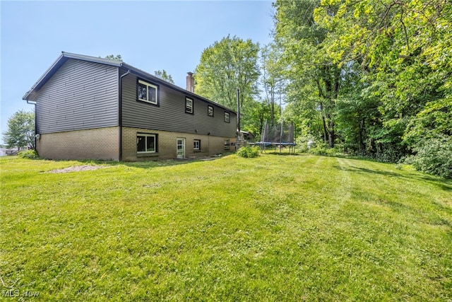 11996 Bower Rd, Minerva, OH 44657 - back of house featuring a trampoline, a chimney, a lawn, and brick siding