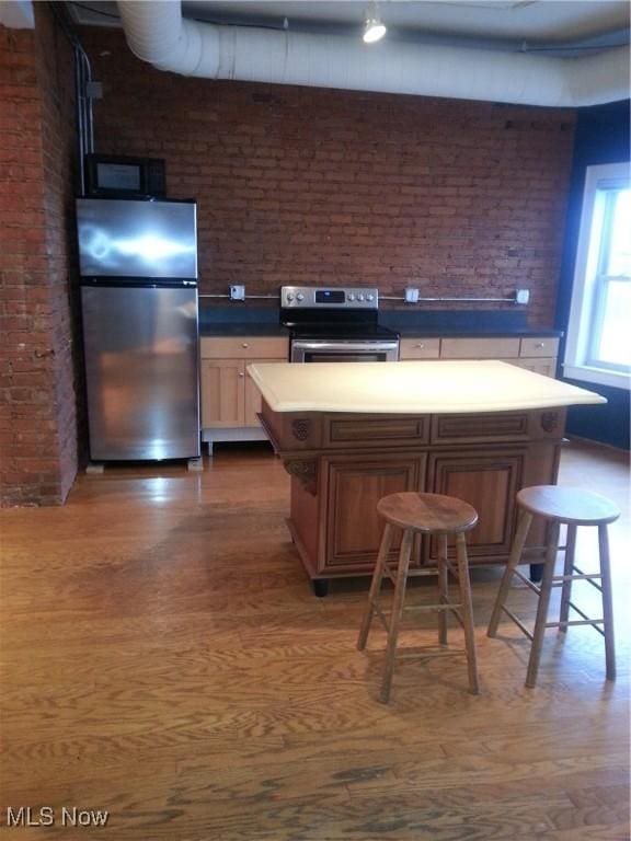 1401 W 75th St Unit D, Cleveland, OH 44102 - kitchen with appliances with stainless steel finishes, brick wall, a center island, wood finished floors, and a kitchen breakfast bar