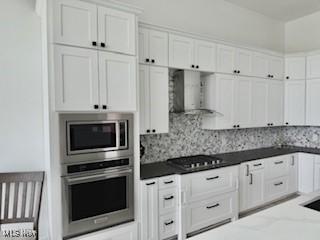 5771 E Blvd NW, Canton, OH 44718 - kitchen featuring appliances with stainless steel finishes, wall chimney exhaust hood, white cabinets, tasteful backsplash, and dark countertops