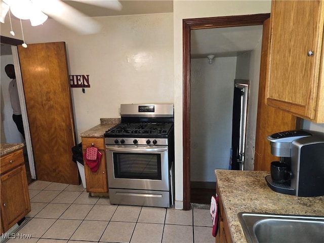22061 Miller Ave, Euclid, OH 44119 - kitchen featuring gas range, light tile patterned floors, ceiling fan, and brown cabinets