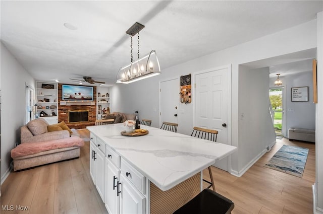 8222 Starburst Rd, Mentor, OH 44060 - kitchen with a ceiling fan, a fireplace, a breakfast bar area, light wood-style flooring, and white cabinets