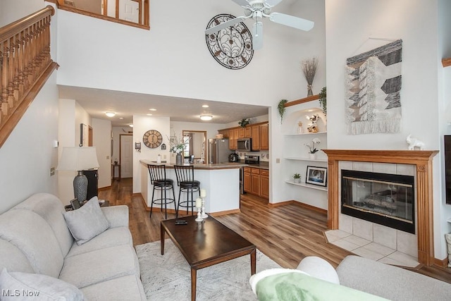 2401 Bunker Ln Unit B, Willoughby, OH 44094 - living room featuring a towering ceiling, light wood finished floors, ceiling fan, a tile fireplace, and baseboards