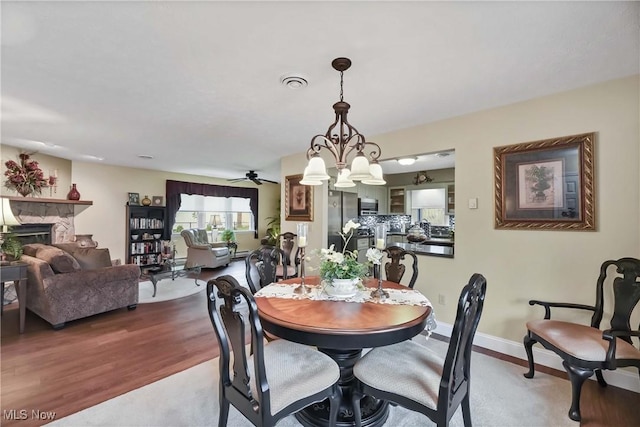1421 Rolling Meadows Dr, Vermilion, OH 44089 - dining room with a stone fireplace, a ceiling fan, wood finished floors, baseboards, and a chandelier