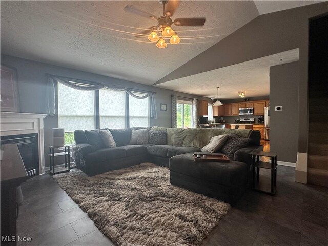 2280 Becket Cir, Stow, OH 44224 - living area with a textured ceiling, vaulted ceiling, dark tile patterned flooring, a glass covered fireplace, and a ceiling fan