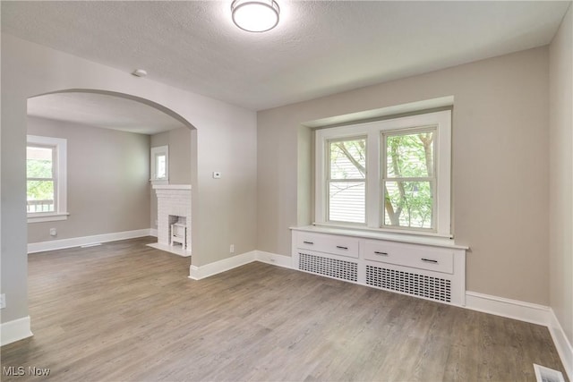 1260 Beardsley St, Akron, OH 44301 - empty room with wood finished floors, baseboards, arched walkways, a textured ceiling, and a brick fireplace