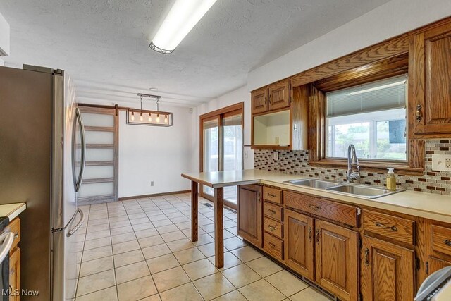 1825 E Skyline Dr, Lorain, OH 44053 - kitchen featuring a sink, backsplash, brown cabinetry, freestanding refrigerator, and light countertops