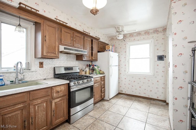 7428 Ira Ave, Brooklyn, OH 44144 - kitchen with stainless steel gas range oven, extractor fan, freestanding refrigerator, brown cabinets, and wallpapered walls