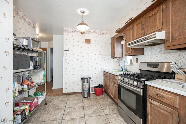 7428 Ira Ave, Brooklyn, OH 44144 - kitchen featuring stainless steel gas range oven, under cabinet range hood, wallpapered walls, light countertops, and brown cabinets