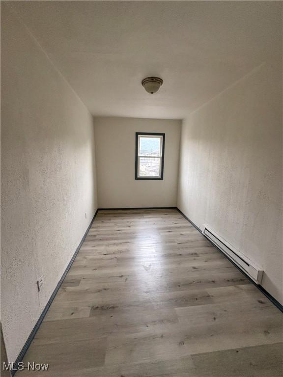 1019 Commerce St, Wellsville, OH 43968 - empty room featuring a baseboard heating unit, a textured wall, and light wood-style floors