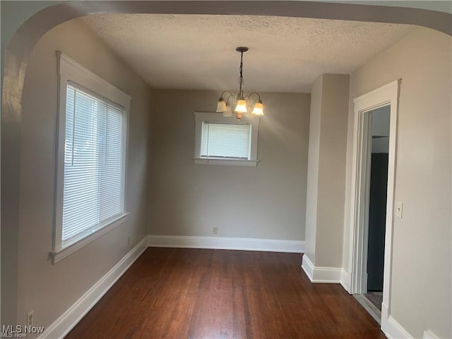 3961 E 53rd St, Newburgh Heights, OH 44105 - unfurnished dining area featuring dark wood finished floors, a chandelier, a textured ceiling, baseboards, and arched walkways