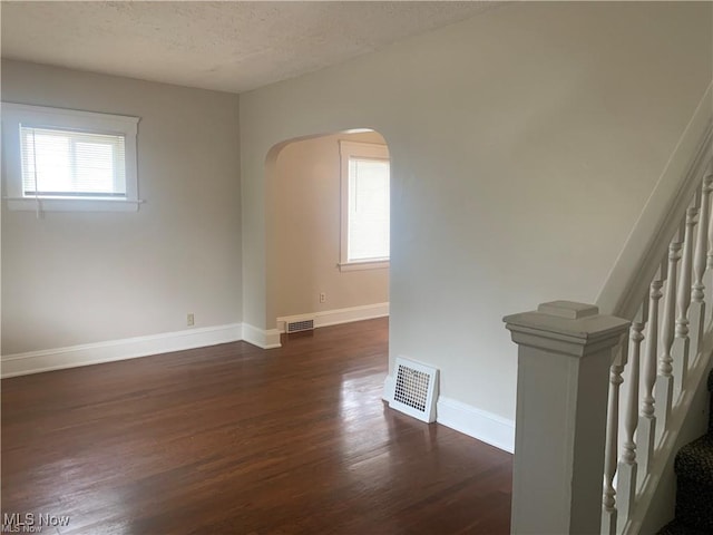 3961 E 53rd St, Newburgh Heights, OH 44105 - empty room with arched walkways, dark wood-type flooring, baseboards, a textured ceiling, and stairway