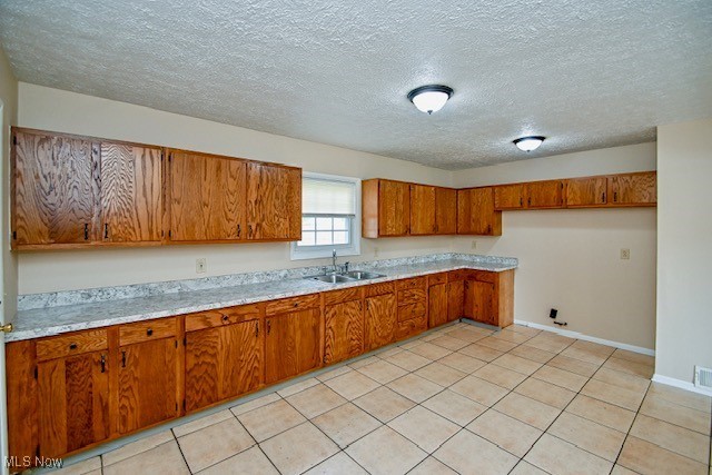 2312 Midway Ave NE, Canton, OH 44705 - kitchen with brown cabinetry, a sink, light countertops, a textured ceiling, and light tile patterned flooring