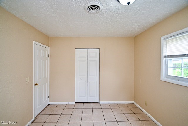 2312 Midway Ave NE, Canton, OH 44705 - unfurnished bedroom with a closet, light tile patterned floors, baseboards, and a textured ceiling